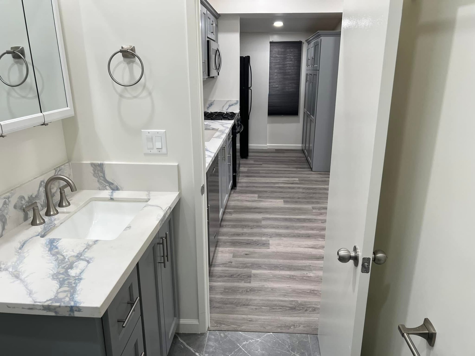 ADU interior showing finished bath vanity with quartz counters and view through to a galley kitchen with stainless appliances